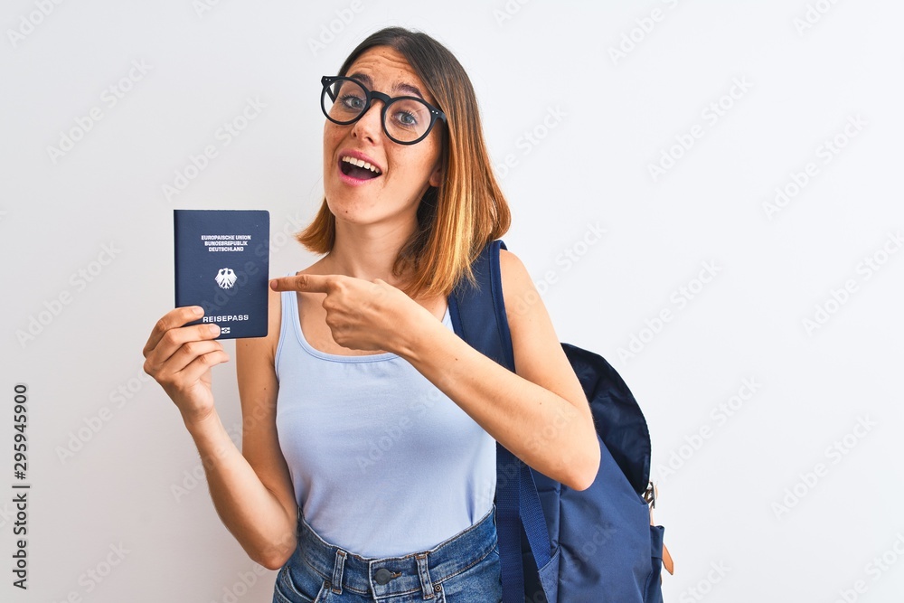 Beautiful redhead student woman wearing backpack and holding passport of germany very happy pointing with hand and finger