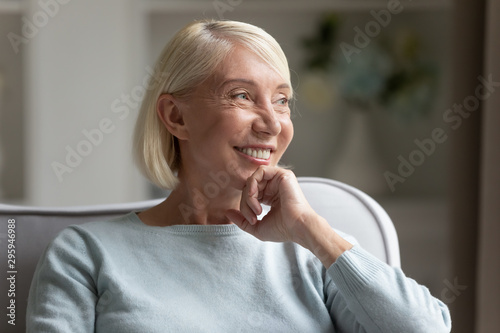 Smiling older woman looking away, dreaming at home.