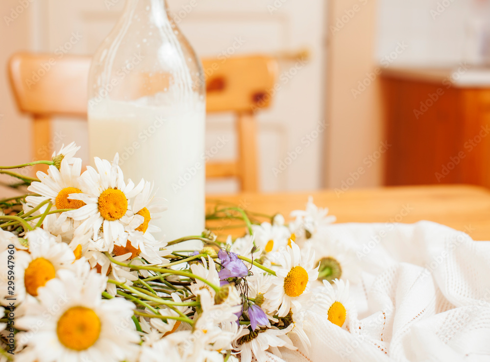 Simply stylish wooden kitchen with bottle of milk and glass on table, summer flowers camomile, healthy foog moring concept close up