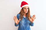 Young beautiful redhead woman wearing christmas hat over isolated background Moving away hands palms showing refusal and denial with afraid and disgusting expression. Stop and forbidden.