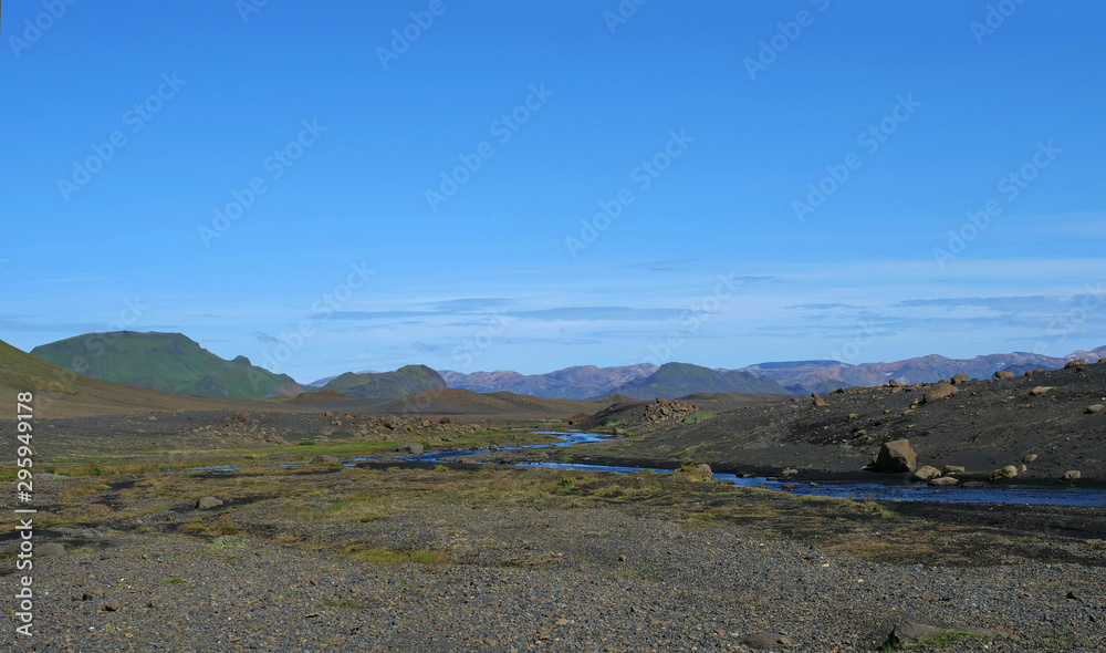 Icelandic lava desert landscape with bending river and panorama of Landmannalaugar colorful mountains and green hills. Fjallabak Nature Reserve, Iceland. Summer blue sky