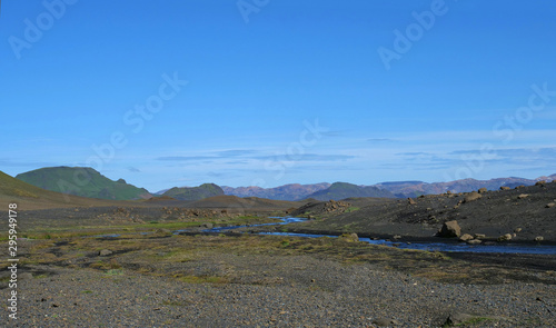 Icelandic lava desert landscape with bending river and panorama of Landmannalaugar colorful mountains and green hills. Fjallabak Nature Reserve, Iceland. Summer blue sky