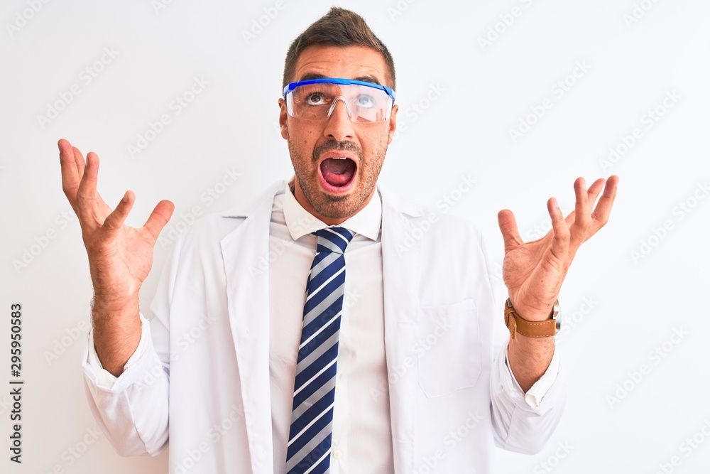 Young handsome scientist man wearing safety glasses over isolated background crazy and mad shouting and yelling with aggressive expression and arms raised. Frustration concept.