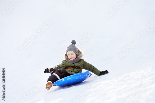 Little boy enjoy riding on ice slide in winter.