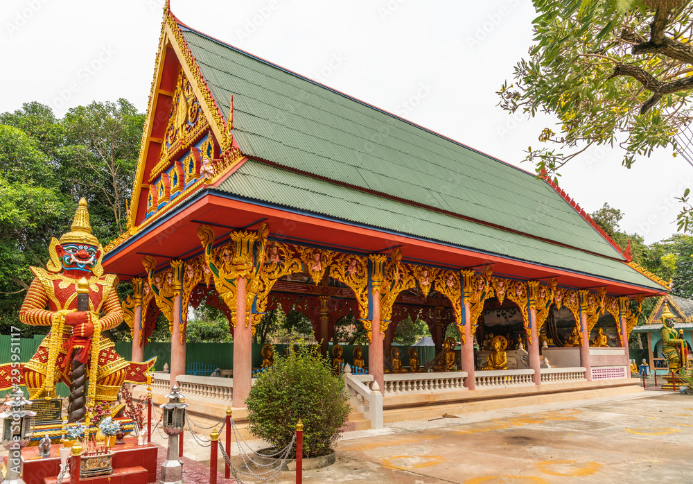 Bang Saen, Thailand - March 16, 2019: Wang Saensuk Buddhist Monastery. Monkey-like dwarapalaka guardian statues on both sides of main open prayer hall under silver sky with green foliage.