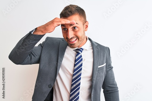 Young handsome business man wearing suit and tie over isolated background very happy and smiling looking far away with hand over head. Searching concept.