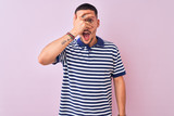 Young handsome man wearing nautical striped t-shirt over pink isolated background peeking in shock covering face and eyes with hand, looking through fingers with embarrassed expression.