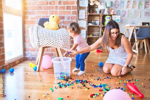 Young beautiful teacher and toddler playing with building blocks toys at kindergarten