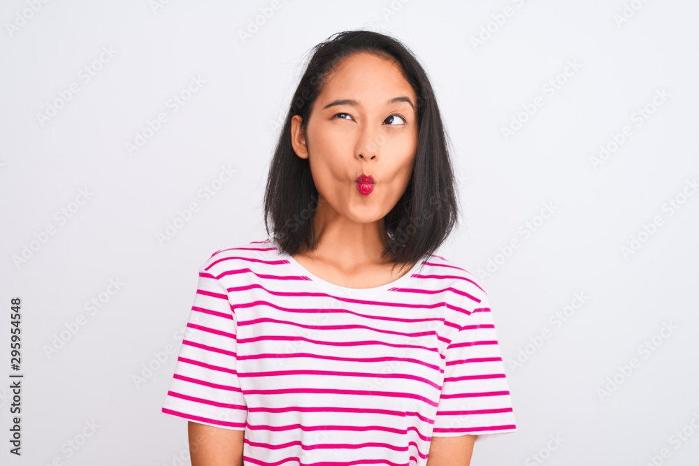 Young chinese woman wearing striped t-shirt standing over isolated white background making fish face with lips, crazy and comical gesture. Funny expression.
