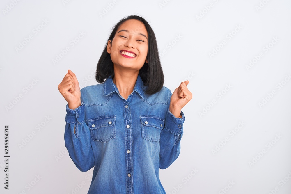 Εκτύπωση καμβά Young beautiful chinese woman wearing denim shirt standing over isolated white background excited for success with arms raised and eyes closed celebrating victory smiling