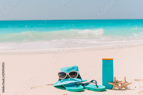 Suncream bottles, sunglasses, flip flop on white sand background ocean
