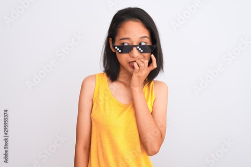 Young beautiful chinese woman wearing thug life sunglasses over isolated white background looking stressed and nervous with hands on mouth biting nails. Anxiety problem.