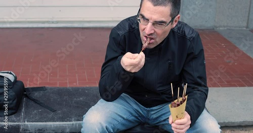 A man eats sheep skewers on the street photo