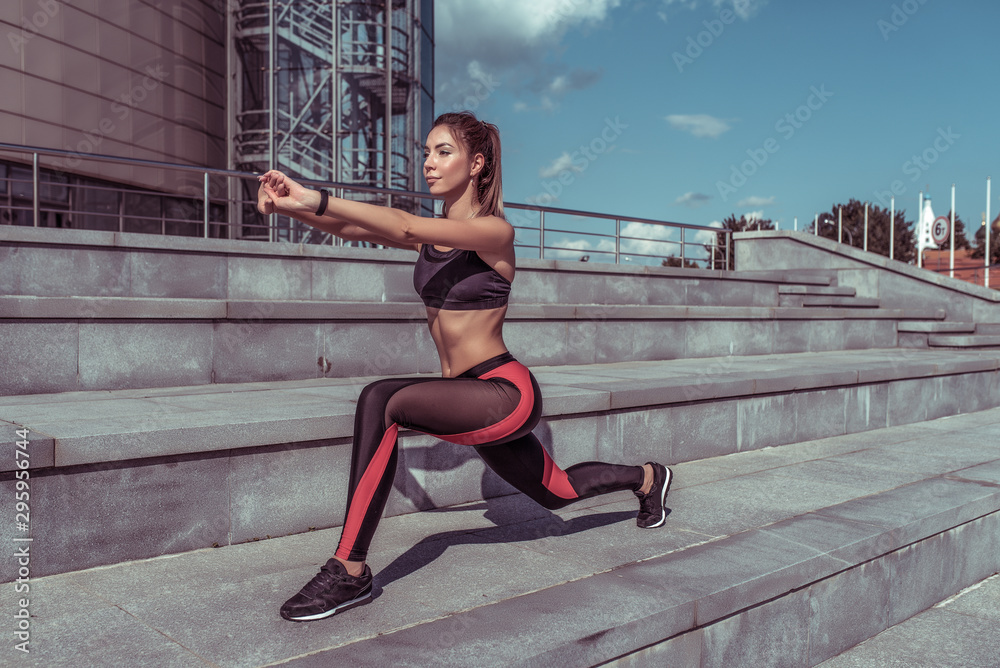 Girl athlete in summer in city does stretching and gymnastics. Workout before morning jogging, fitness outdoor workout. Tanned and slim figure, motivation for woman lifestyle.