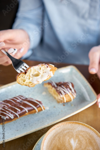 A young woman drinks coffee cappuccino in a restaurant and eats dessert. Traditional french eclairs with chocolate. Cake decorated with vanilla cream and chocolate frosting.