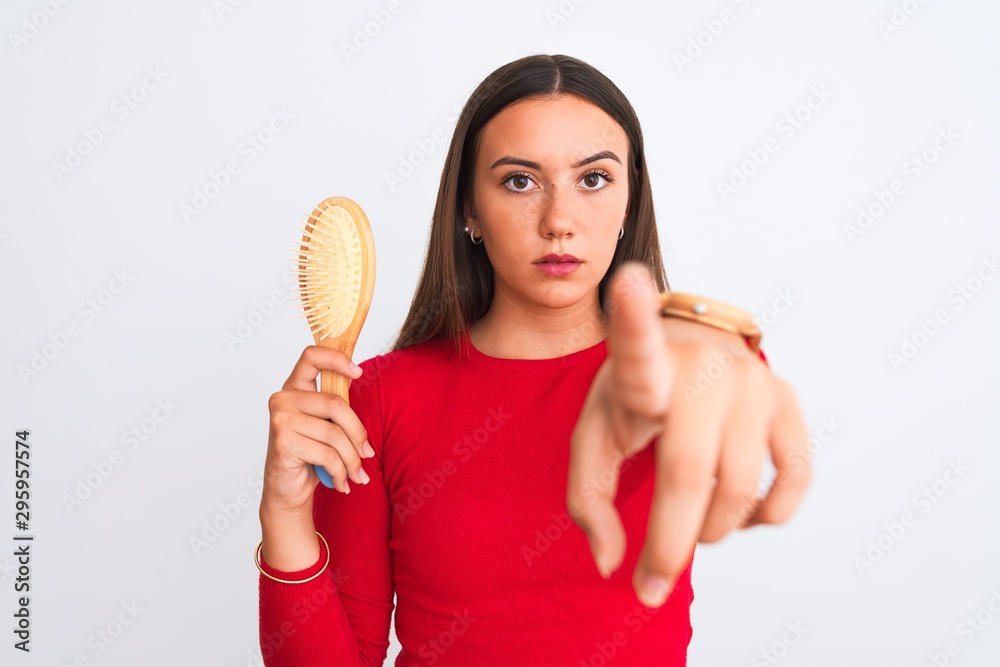Young beautiful girl holding hair comb standing over isolated white background pointing with finger to the camera and to you, hand sign, positive and confident gesture from the front Young beautiful girl holding hair comb standing over isolated white background pointing with finger to the camera and to you, hand sign, positive and confident gesture from the front