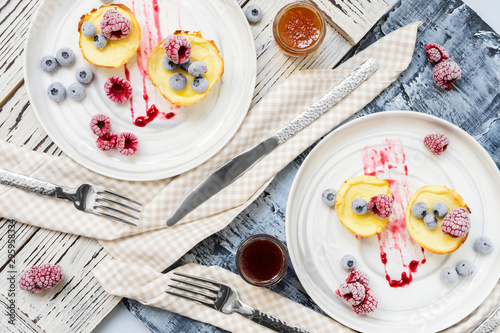 Delicious homemade cheese pancakes, cheesecakes, syrniki with fresh blueberry, raspberry and jam, napkin, fork on black wooden backdrop. Breakfast restaurant menu. Diet natural food flat lay concept.