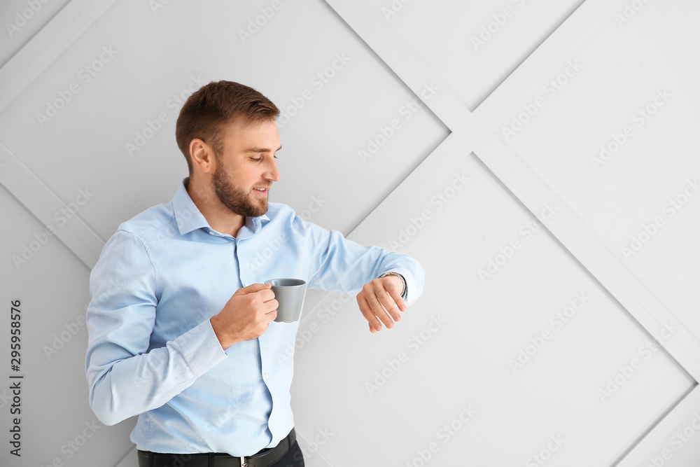 Portrait of handsome businessman with cup of coffee looking at watch on light background Portrait of handsome businessman with cup of coffee looking at watch on light background