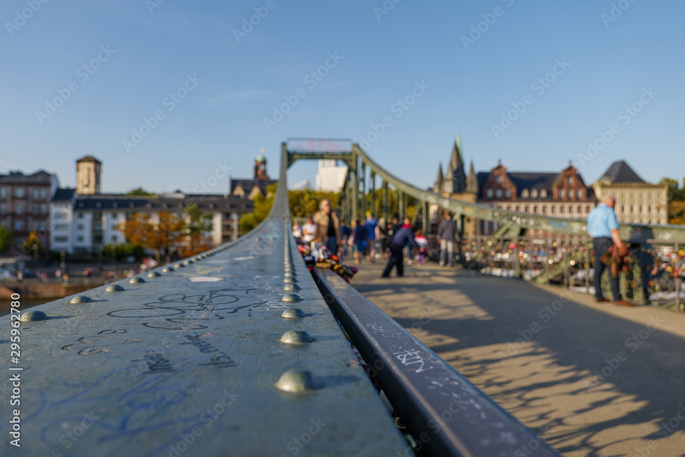 Close up view on steel handrail of balustrade on footbridge called Iron Bridge, Eiserner Steg, cross Main River in Frankfurt, Germany and blur background crowd of tourists. Close up view on steel handrail of balustrade on footbridge called Iron Bridge, Eiserner Steg, cross Main River in Frankfurt, Germany and blur background crowd of tourists.