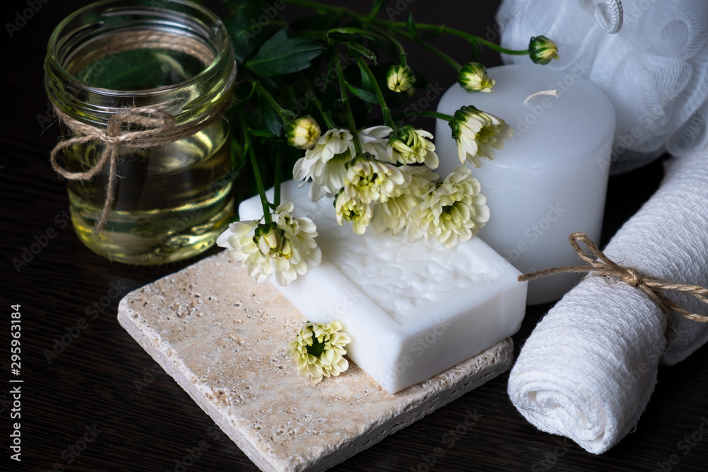 Handmade soap with a pattern lies on the table.  On a white table is handmade soap, flowers and olive oil.  Collection of items for the bathroom