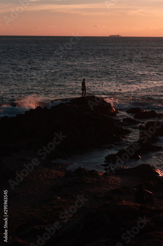 Man contemplating the sunset on rocks in the sea