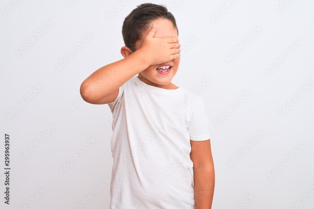 Beautiful kid boy wearing casual t-shirt standing over isolated white background smiling and laughing with hand on face covering eyes for surprise. Blind concept. Beautiful kid boy wearing casual t-shirt standing over isolated white background smiling and laughing with hand on face covering eyes for surprise. Blind concept.
