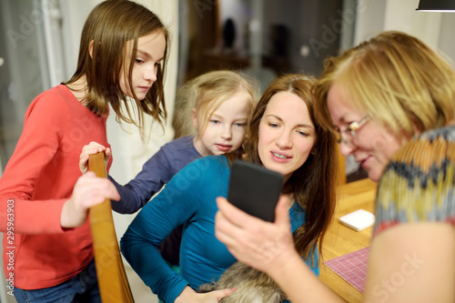Fototapeta Naklejka Na Ścianę i Meble -  Beautiful family with young children using a smartphone and smiling while sitting by the table at home. Mom, grandma and kids making a call using a phone.