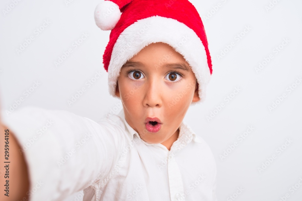 Beautiful kid boy wearing Christmas Santa hat make selfie over isolated white background scared in shock with a surprise face, afraid and excited with fear expression Beautiful kid boy wearing Christmas Santa hat make selfie over isolated white background scared in shock with a surprise face, afraid and excited with fear expression