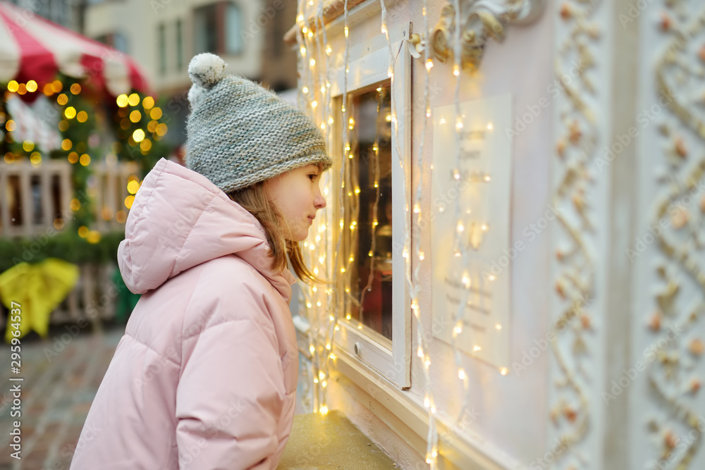 Cute young girl choosing sweets on traditional Christmas market in Riga, Latvia. Kid buying candy and cookies on Xmas.