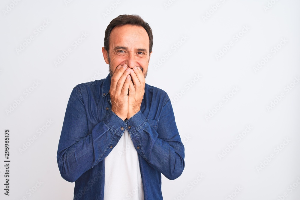 Middle age handsome man wearing blue denim shirt standing over isolated white background laughing and embarrassed giggle covering mouth with hands, gossip and scandal concept Middle age handsome man wearing blue denim shirt standing over isolated white background laughing and embarrassed giggle covering mouth with hands, gossip and scandal concept