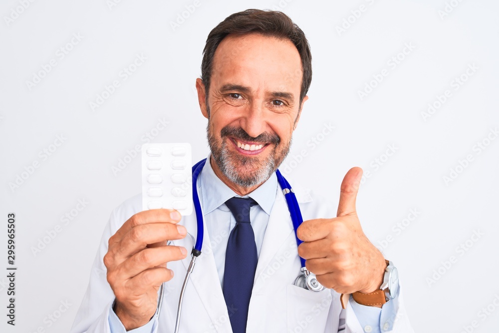 Middle age doctor man holding pills standing over isolated white background happy with big smile doing ok sign, thumb up with fingers, excellent sign Middle age doctor man holding pills standing over isolated white background happy with big smile doing ok sign, thumb up with fingers, excellent sign