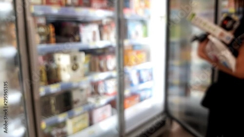 Woman opening supermarket fridge to take frozen food. Out of focus