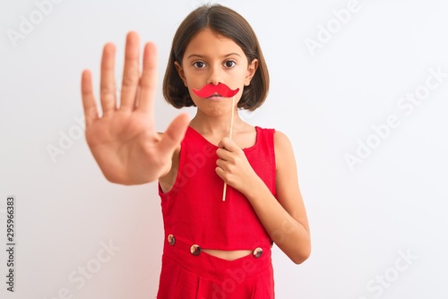 Beautiful child girl holding fanny party mustache standing over isolated white background with open hand doing stop sign with serious and confident expression  defense gesture