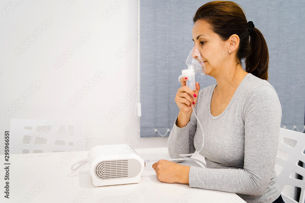 Portrait of adult woman using steam vapor inhaler nebulizer doing aerosol inhalation medicine treatment at home or hospital flu and asthma bronchitis virus healing Portrait of adult woman using steam vapor inhaler nebulizer doing aerosol inhalation medicine treatment at home or hospital flu and asthma bronchitis virus healing