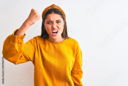 Young beautiful woman wearing yellow sweater and diadem over isolated white background angry and mad raising fist frustrated and furious while shouting with anger. Rage and aggressive concept. © Krakenimages.com