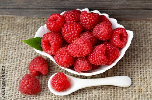 Freshly picked raspberries in a white bowl on a burlap cloth background.Healthy food concept.Selective focus.