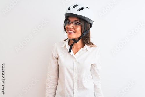 Beautiful businesswoman wearing glasses and bike helmet over isolated white background looking away to side with smile on face, natural expression. Laughing confident.