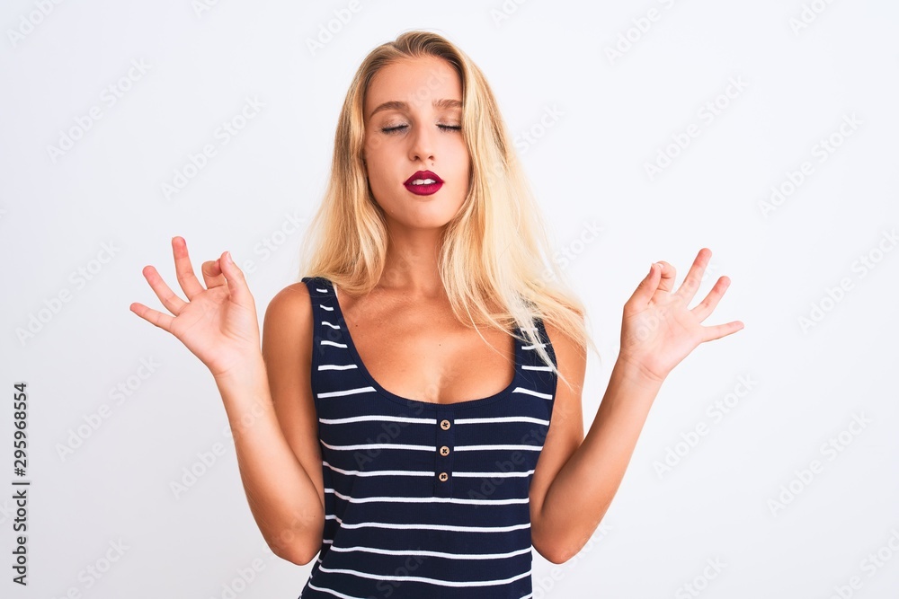 Young beautiful woman wearing casual striped t-shirt standing over isolated white background relax and smiling with eyes closed doing meditation gesture with fingers. Yoga concept. Young beautiful woman wearing casual striped t-shirt standing over isolated white background relax and smiling with eyes closed doing meditation gesture with fingers. Yoga concept.