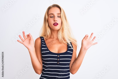 Young beautiful woman wearing casual striped t-shirt standing over isolated white background relax and smiling with eyes closed doing meditation gesture with fingers. Yoga concept.