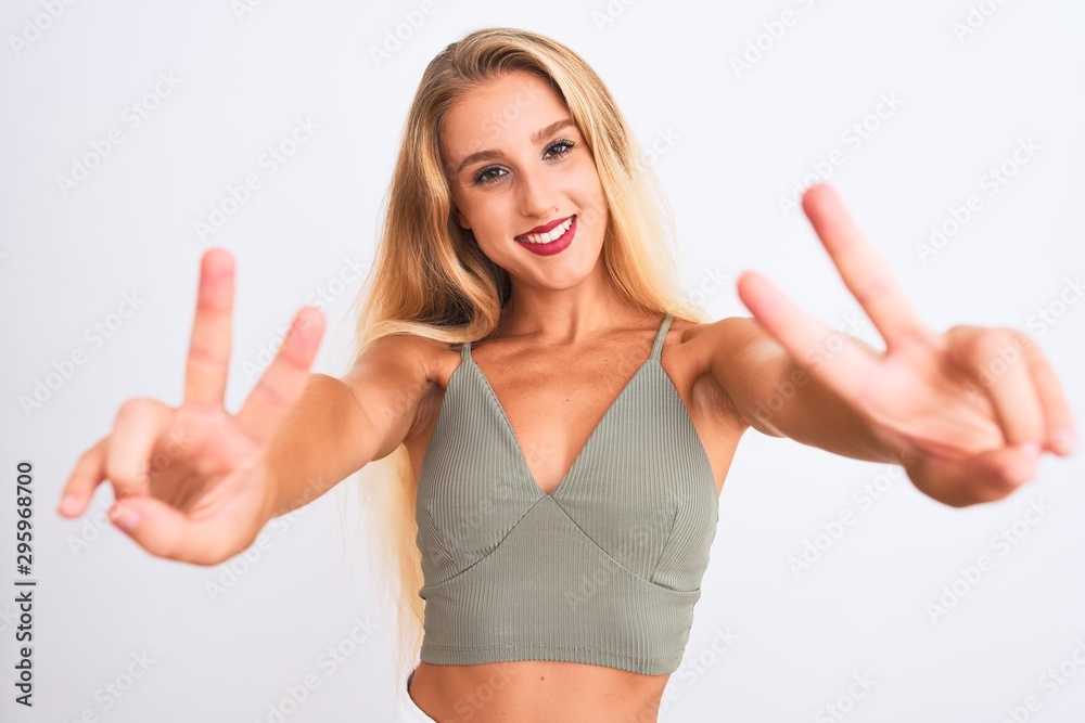 Young beautiful woman wearing casual green t-shirt standing over isolated white background smiling looking to the camera showing fingers doing victory sign. Number two. Young beautiful woman wearing casual green t-shirt standing over isolated white background smiling looking to the camera showing fingers doing victory sign. Number two.