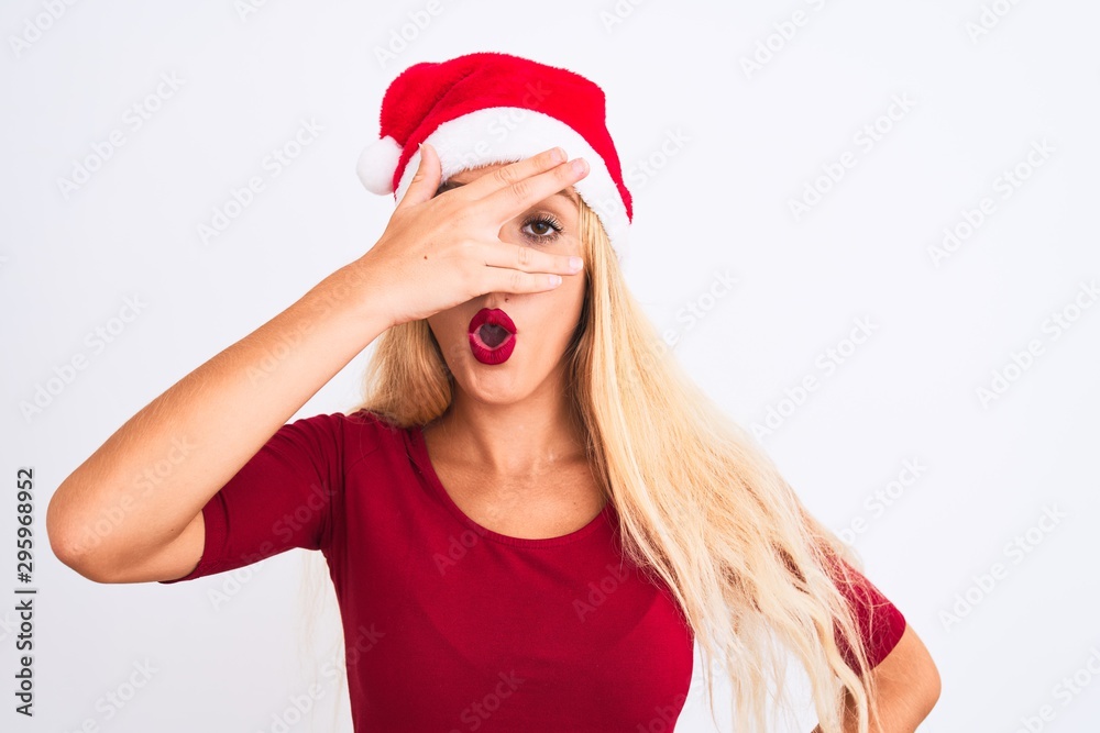 Young beautiful woman wearing Christmas Santa hat over isolated white background peeking in shock covering face and eyes with hand, looking through fingers with embarrassed expression. Young beautiful woman wearing Christmas Santa hat over isolated white background peeking in shock covering face and eyes with hand, looking through fingers with embarrassed expression.