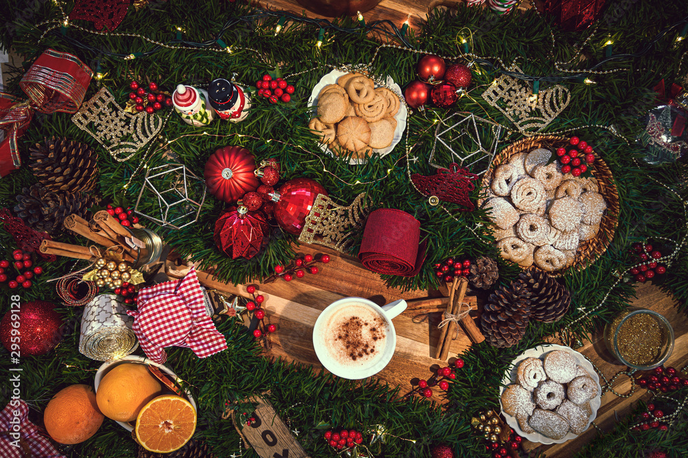 Top View of a cup of Christmas hot chocolate on a table with holiday season ingredients like orange, cookies, panettone, cinnamon and pine