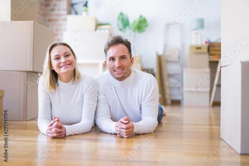 Young beautiful couple lying down on the floor at new home around cardboard boxes