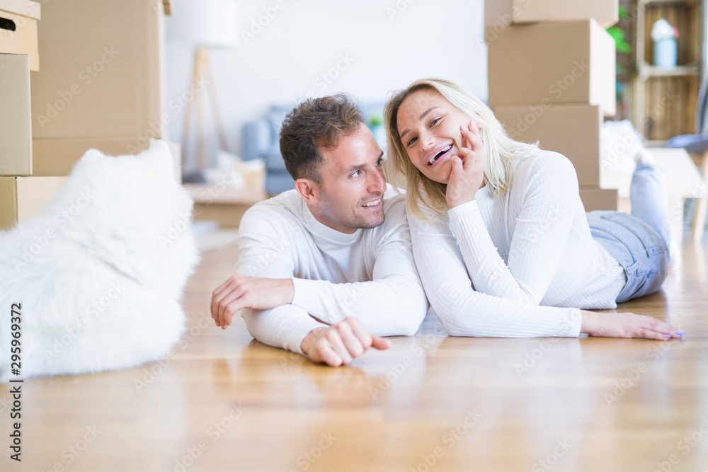 Obraz premium Young beautiful couple with dog lying down on the floor at new home around cardboard boxes
