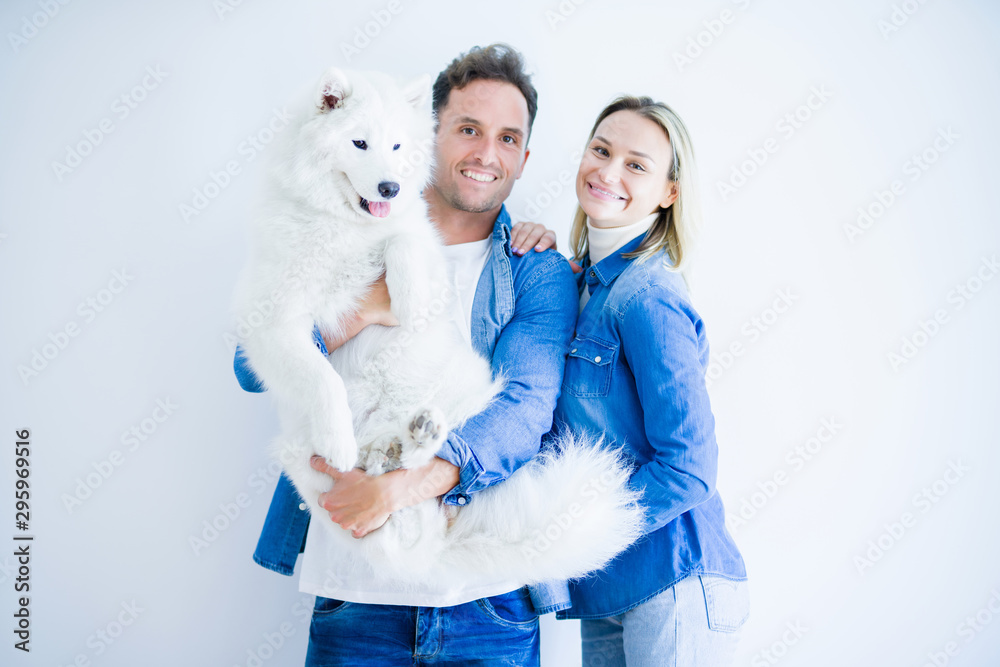 Young beautiful couple holding dog standing over isolated white background Young beautiful couple holding dog standing over isolated white background