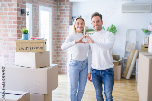Young beautiful couple standing at new home around cardboard boxes smiling in love showing heart symbol and shape with hands. Romantic concept. © Krakenimages.com