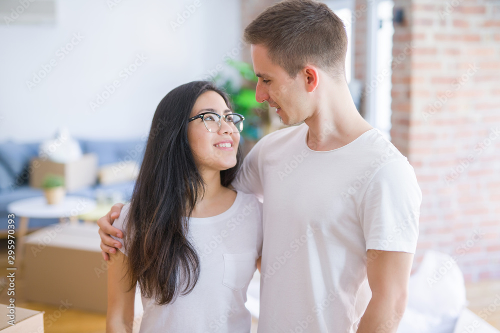 Young beautiful couple standing at new home around cardboard boxes Young beautiful couple standing at new home around cardboard boxes