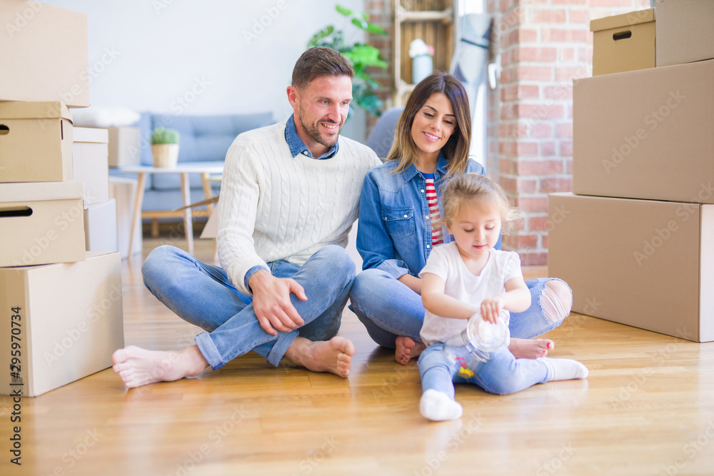 Beautiful family sitting on the floor playing with his kid at new home around cardboard boxes