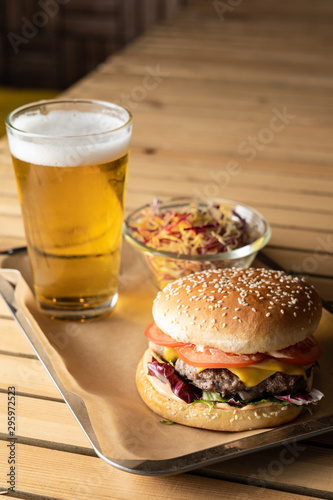 Classic hamburger with cheddar cheese and light lager beer on wooden table