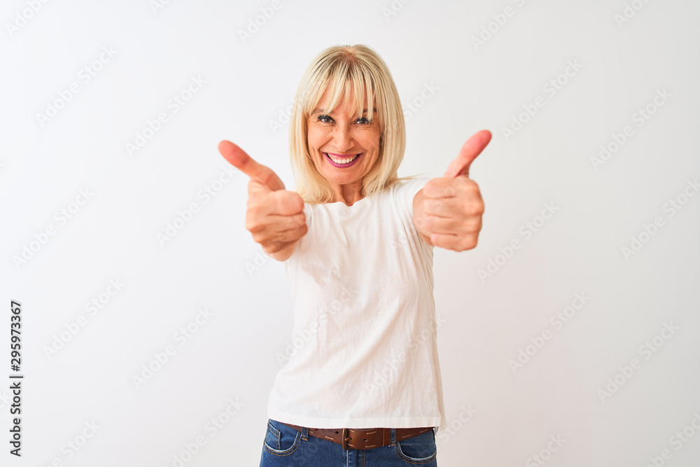 Middle age woman wearing casual t-shirt standing over isolated white background success sign doing positive gesture with hand, thumbs up smiling and happy. Cheerful expression and winner gesture. Middle age woman wearing casual t-shirt standing over isolated white background success sign doing positive gesture with hand, thumbs up smiling and happy. Cheerful expression and winner gesture.